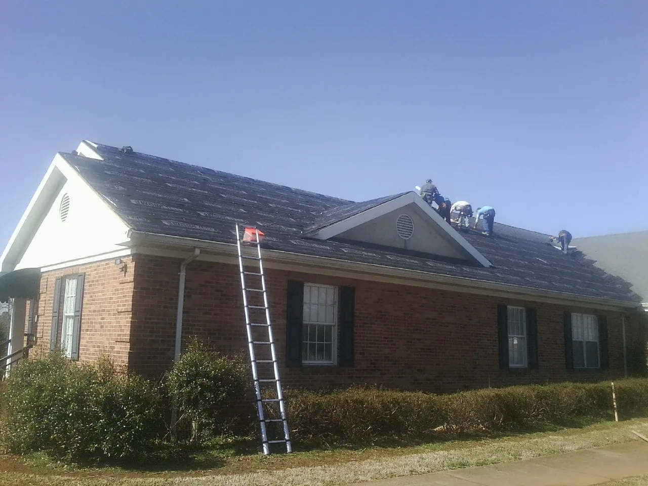 Crew tearing shingles off a brick ranch roof with a ladder set — Metal Roof Repair work by our crew in Alexis