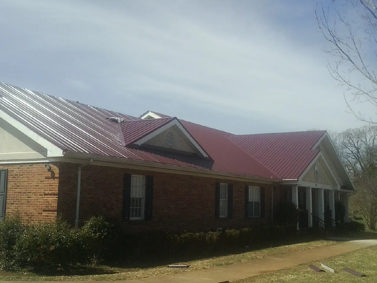 Red metal roof with gabled entries on a long brick building, from a Hail Damage Roof Repair job in Alexis