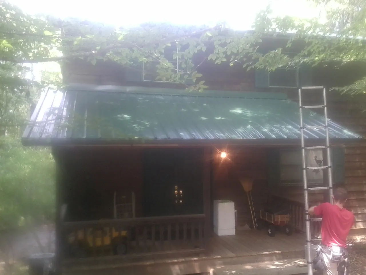 Worker on a ladder at the green porch roof of a wooded cabin in Alexis