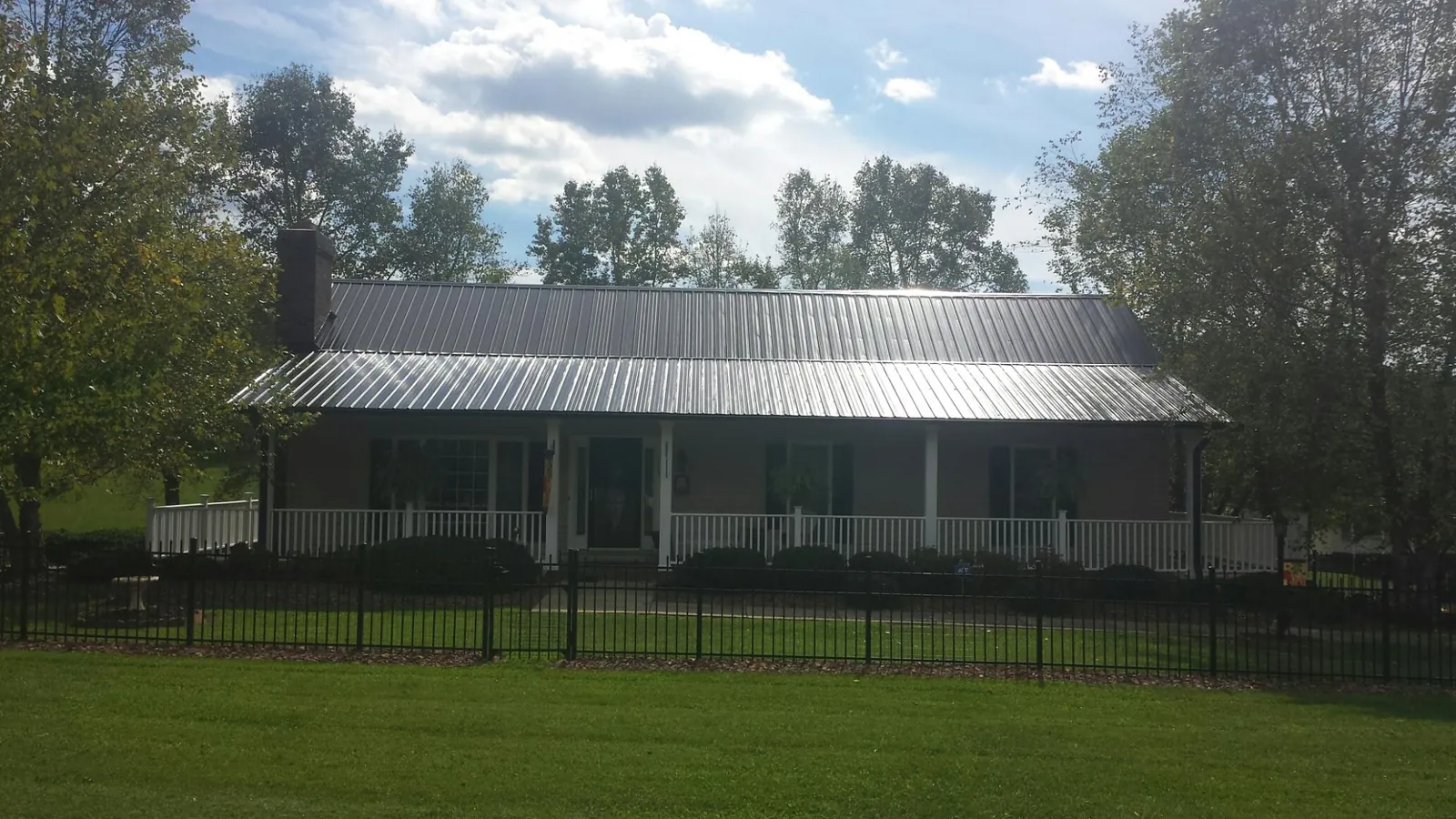 Gray metal roof on a brick ranch with a full width front porch — Gutter Guard Installation work by our crew in Alexis