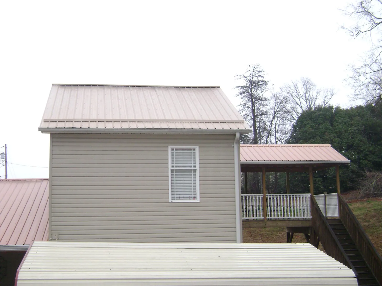 Tan metal roofs on a two story addition and attached porch, from a Roof Replacement job in Alexis